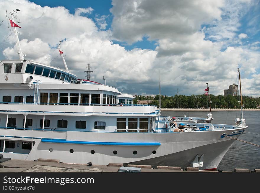 White cruise liner is moored in river port. Saint-Petersburg, Neva river. Blue sky with clouds.