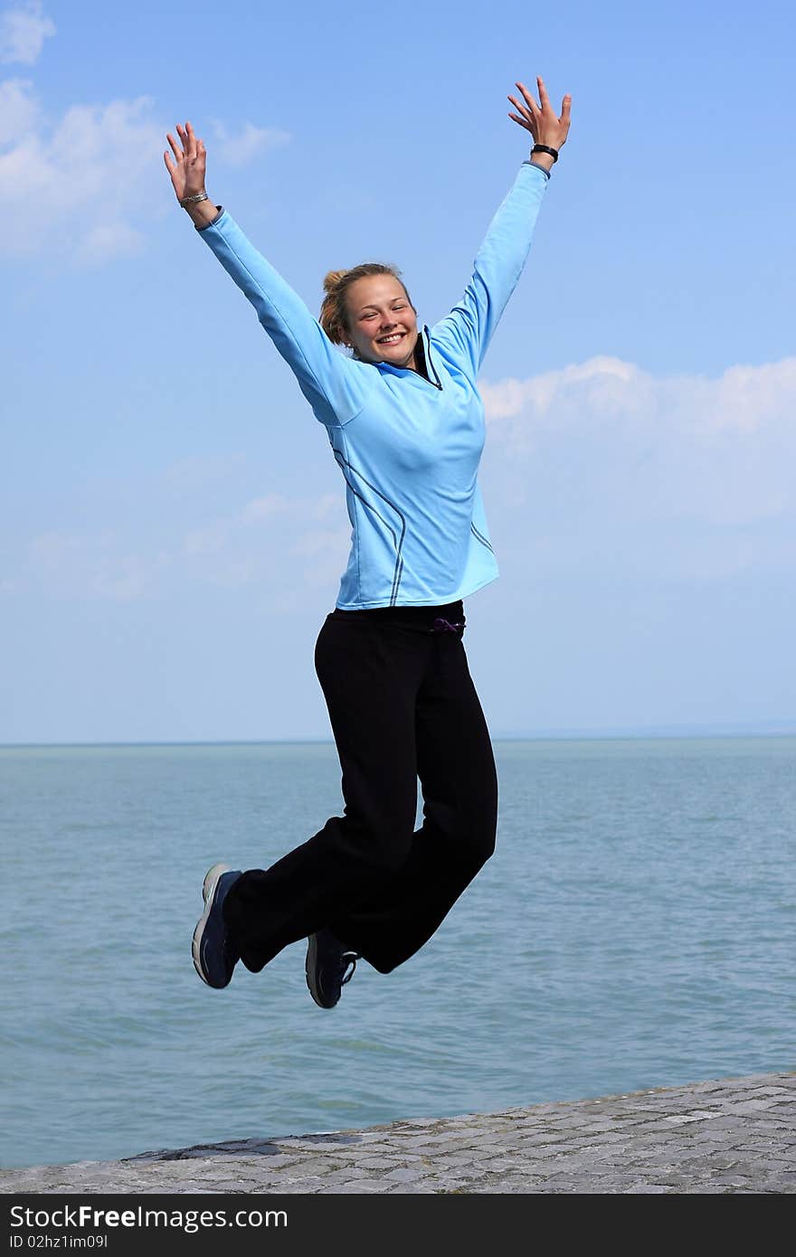 Happy young girl jumping  on the shore