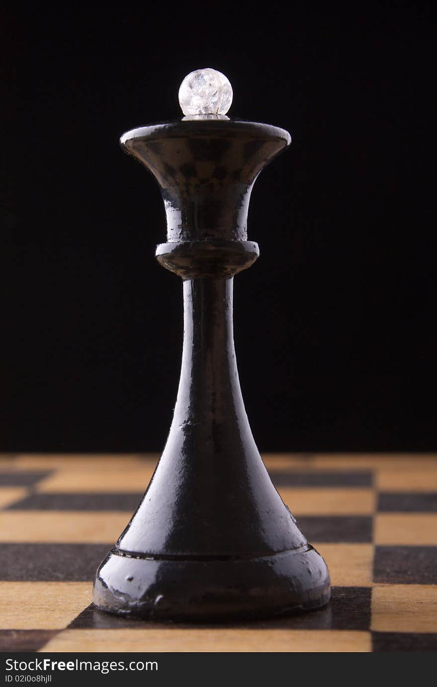 Black chess queen stands on a chessboard, black background