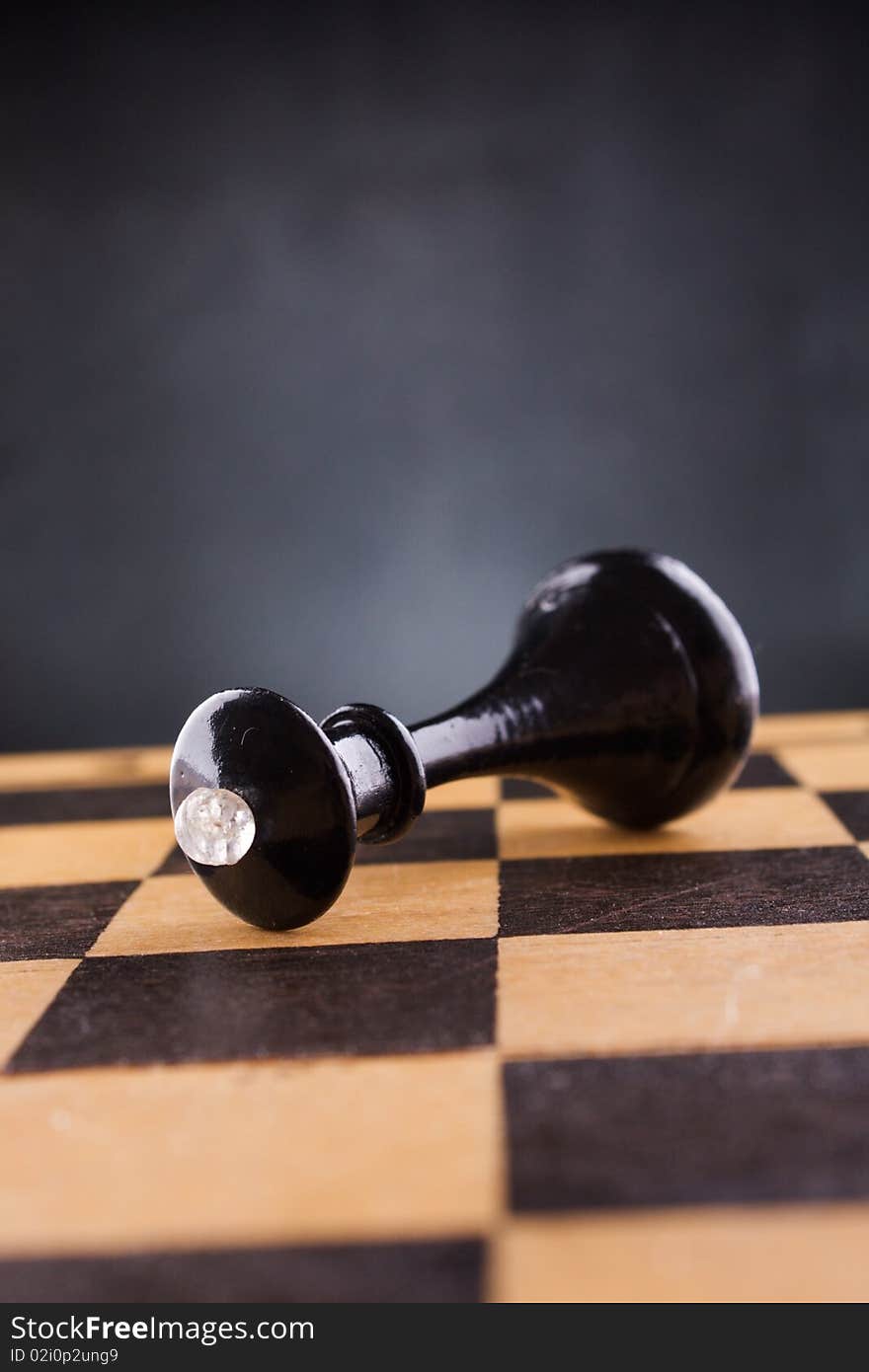 Black chess queen lays on a chessboard, black background