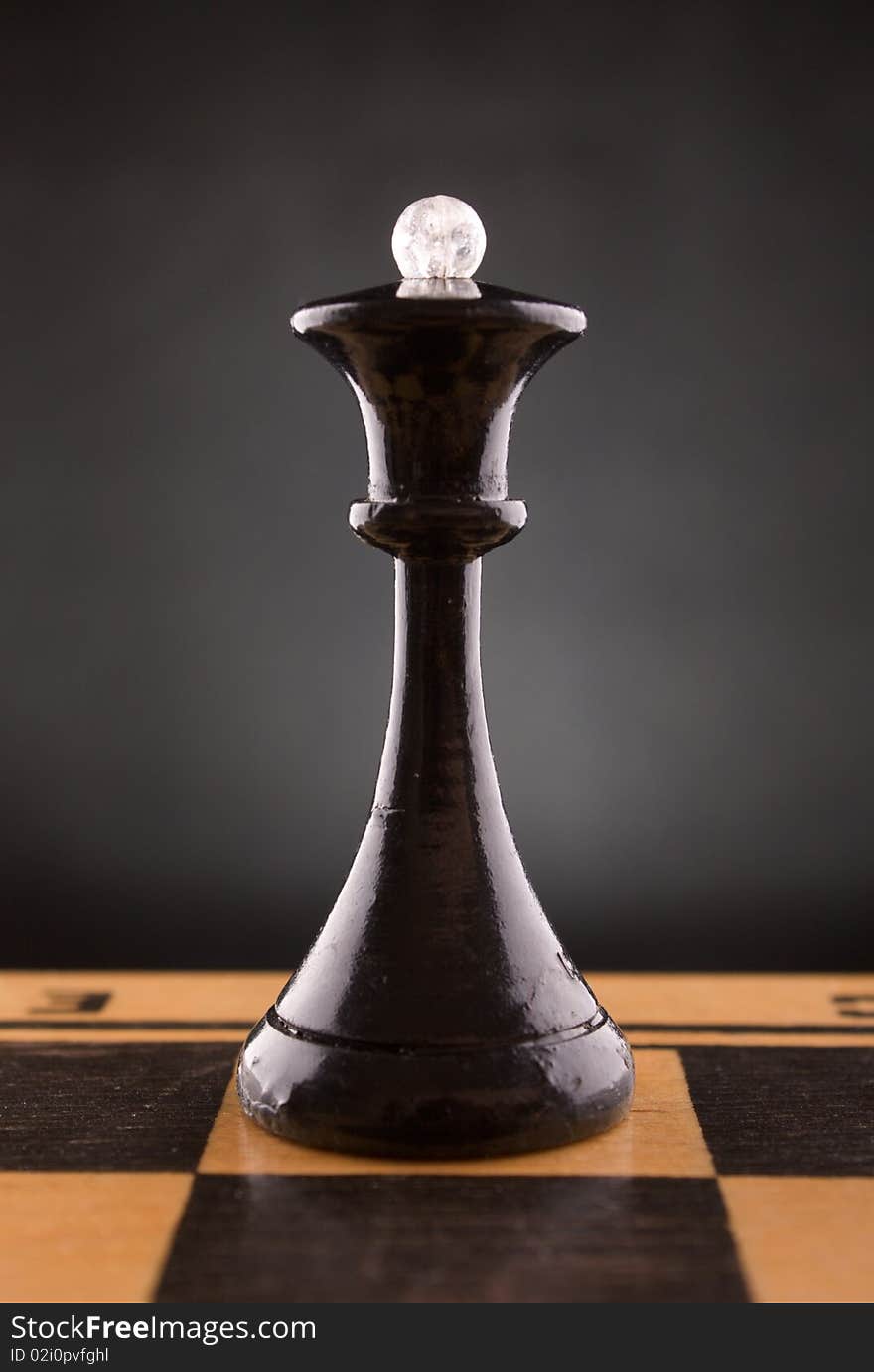 Black chess queen stands on a chessboard, black background