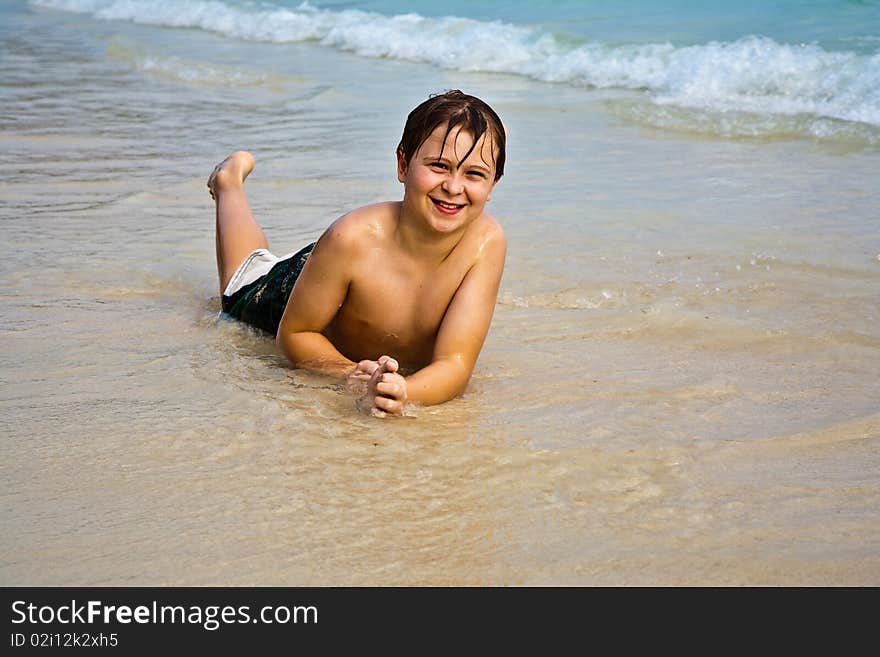 Young boy is lying at the beach and enjoying the warmness of the water and looking self confident and happy. Young boy is lying at the beach and enjoying the warmness of the water and looking self confident and happy