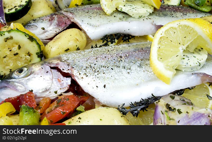 Fresh whole rainbow trouts on a bed of vegetables, ready to be cooked