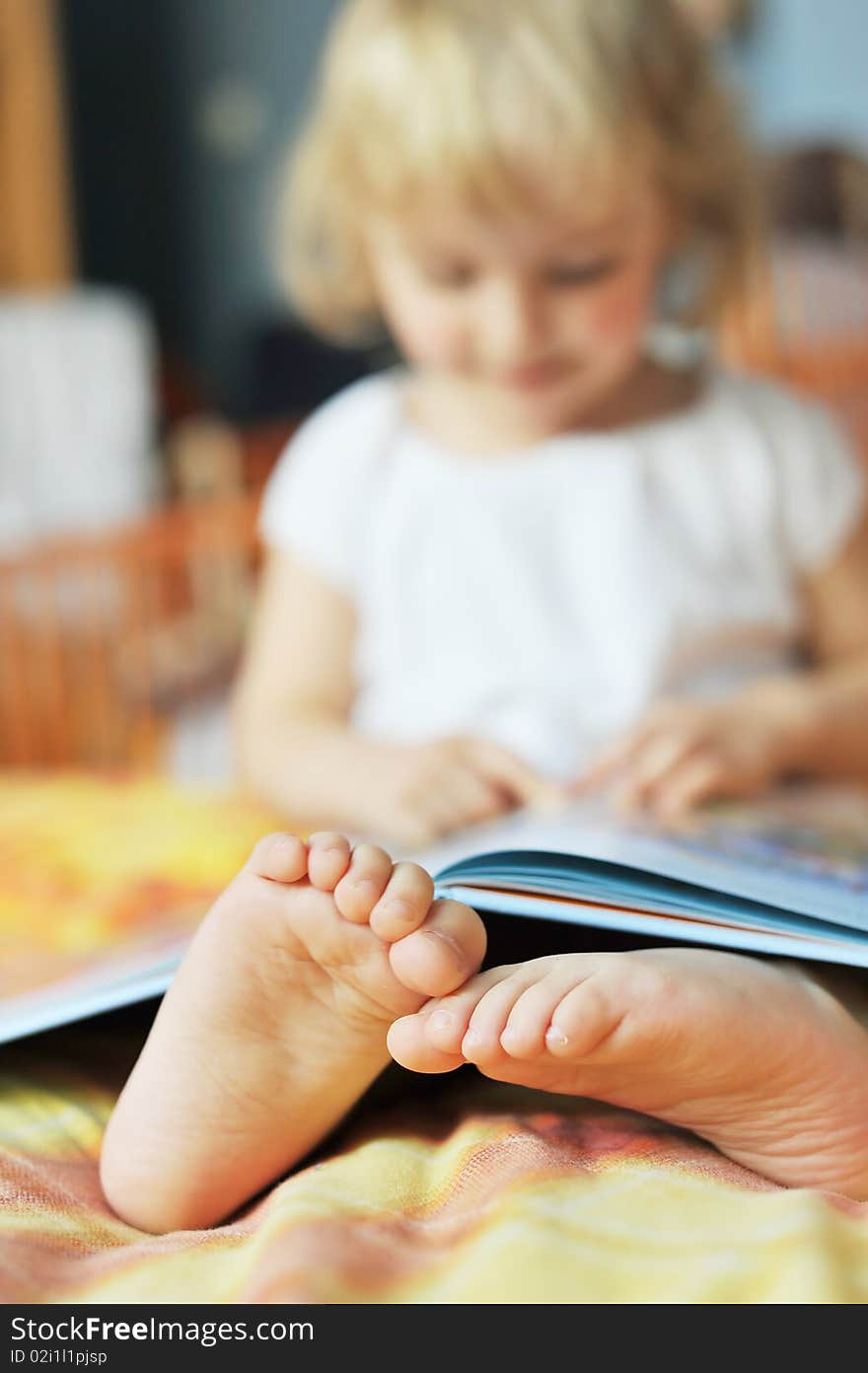 Cheerful little girl with book sits on bed of parents