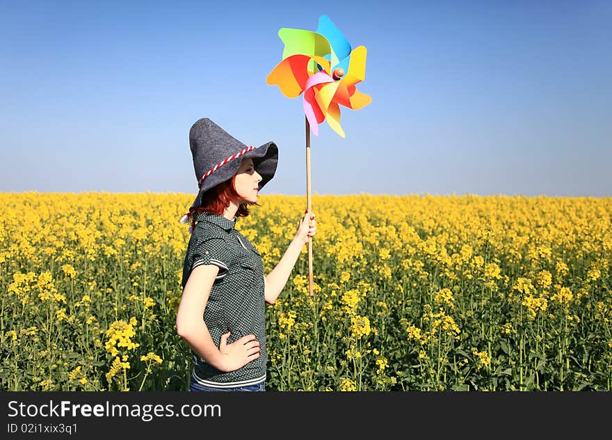 Girl In Cap With Wind Turbine At Rape Field.