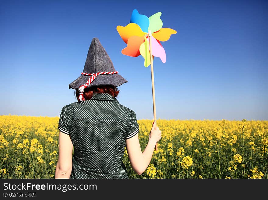 Girl in cap with wind turbine at rape field.