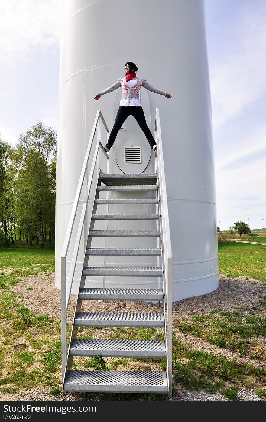 An image of young girl staying on stairs to wind turbine. An image of young girl staying on stairs to wind turbine