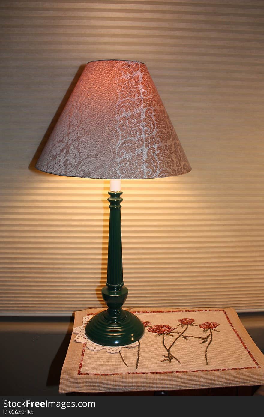 A lit lamp on a small table on top of a mat with flowers.