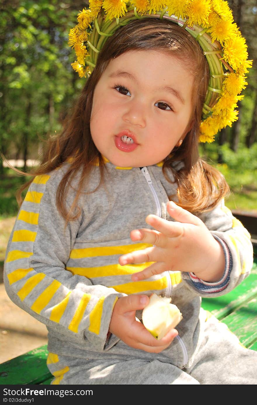 Little girl wearing dandelion diadem eating a slice of apple (talking). Little girl wearing dandelion diadem eating a slice of apple (talking)