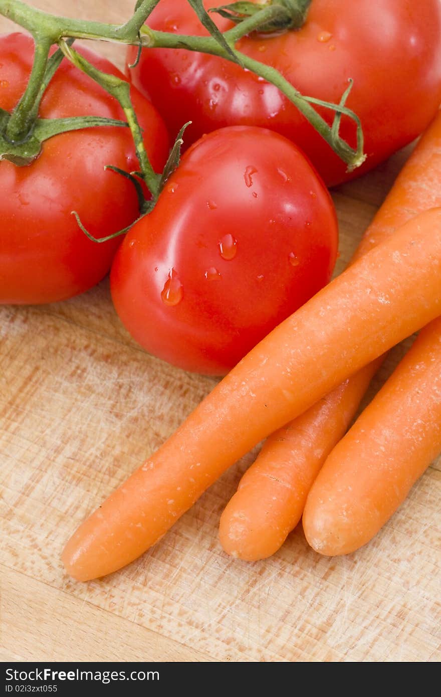 Fresh tomatoes and carrot on wooden cutting board