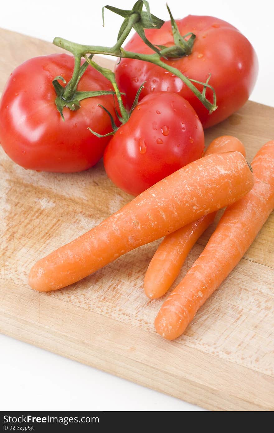 Fresh tomatoes and carrot on wooden cutting board