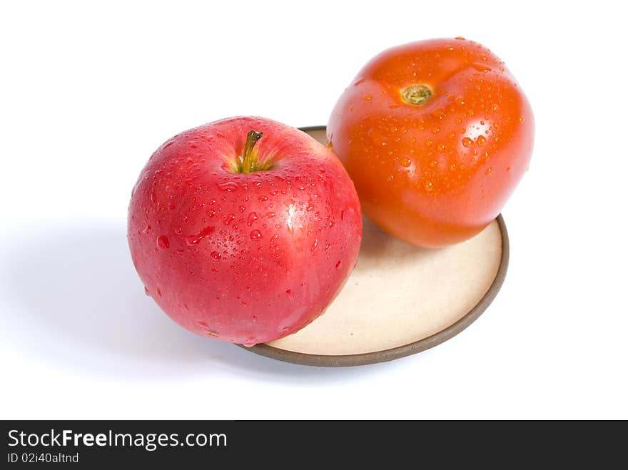 Red ripe tomato and apple, covered with water droplets, on a plate, isolated on white background