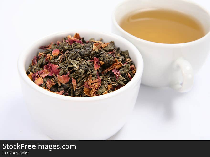 Bowl filled with dried green tea leaves and rose petals and a cup of green tea