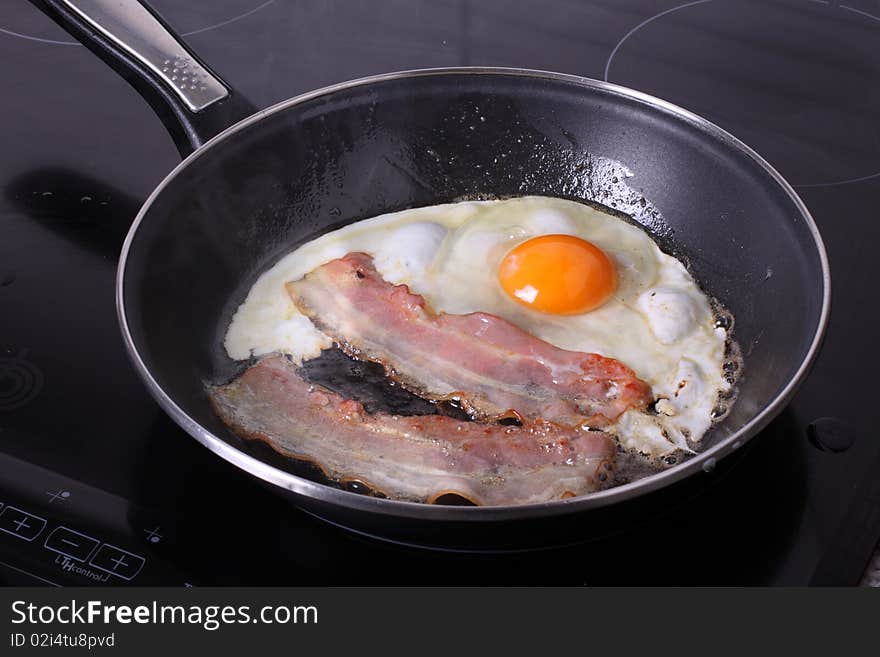 Bacon and eggs being cooked in a fryer