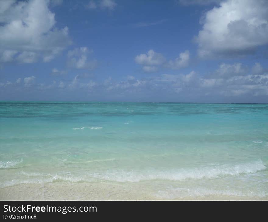 Light blue-green water with off-shore reefs showing underneath blue sky. Light blue-green water with off-shore reefs showing underneath blue sky.