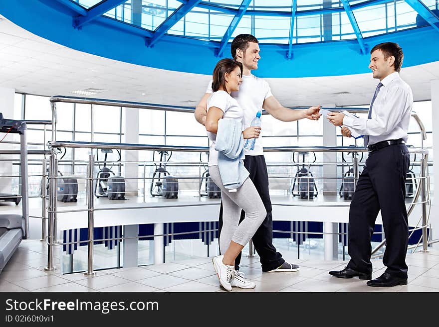 The young couple in sports suits takes cut-away from the manager in sports hall. The young couple in sports suits takes cut-away from the manager in sports hall