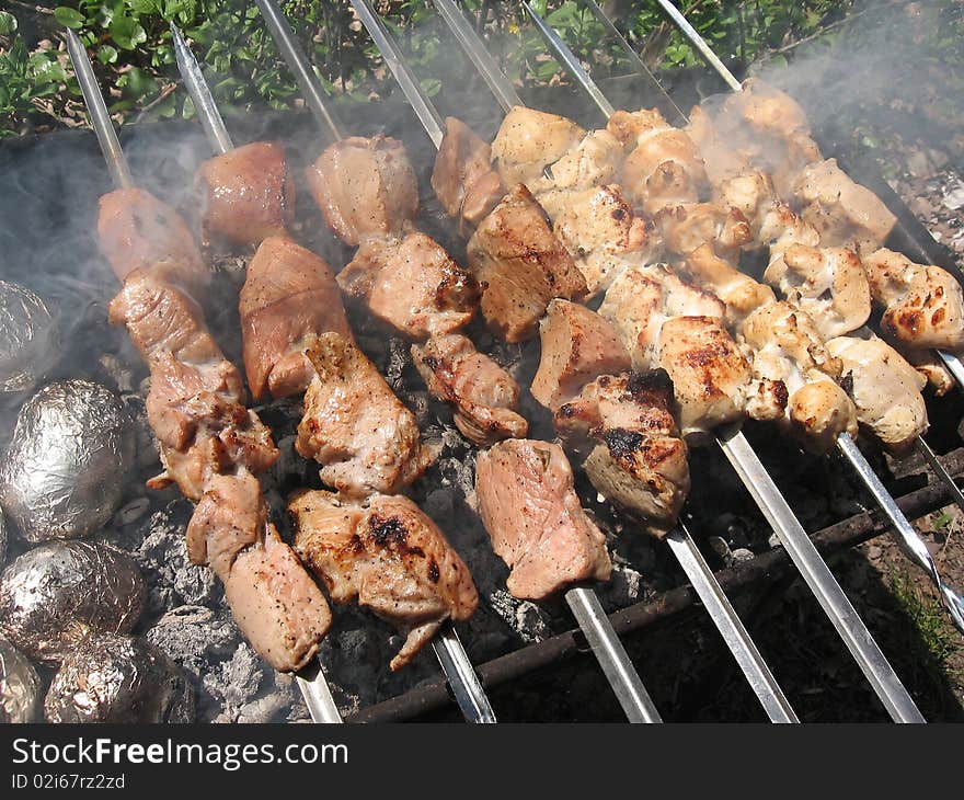 Delicious hot meat skewers on grill and baked potatoes in foil. Delicious hot meat skewers on grill and baked potatoes in foil