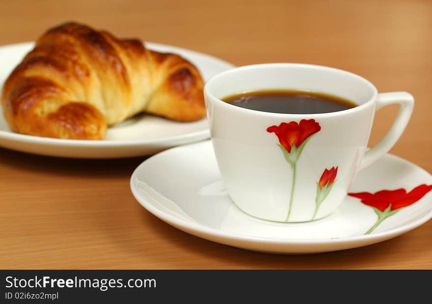 Colorful cup with black coffee and croissant