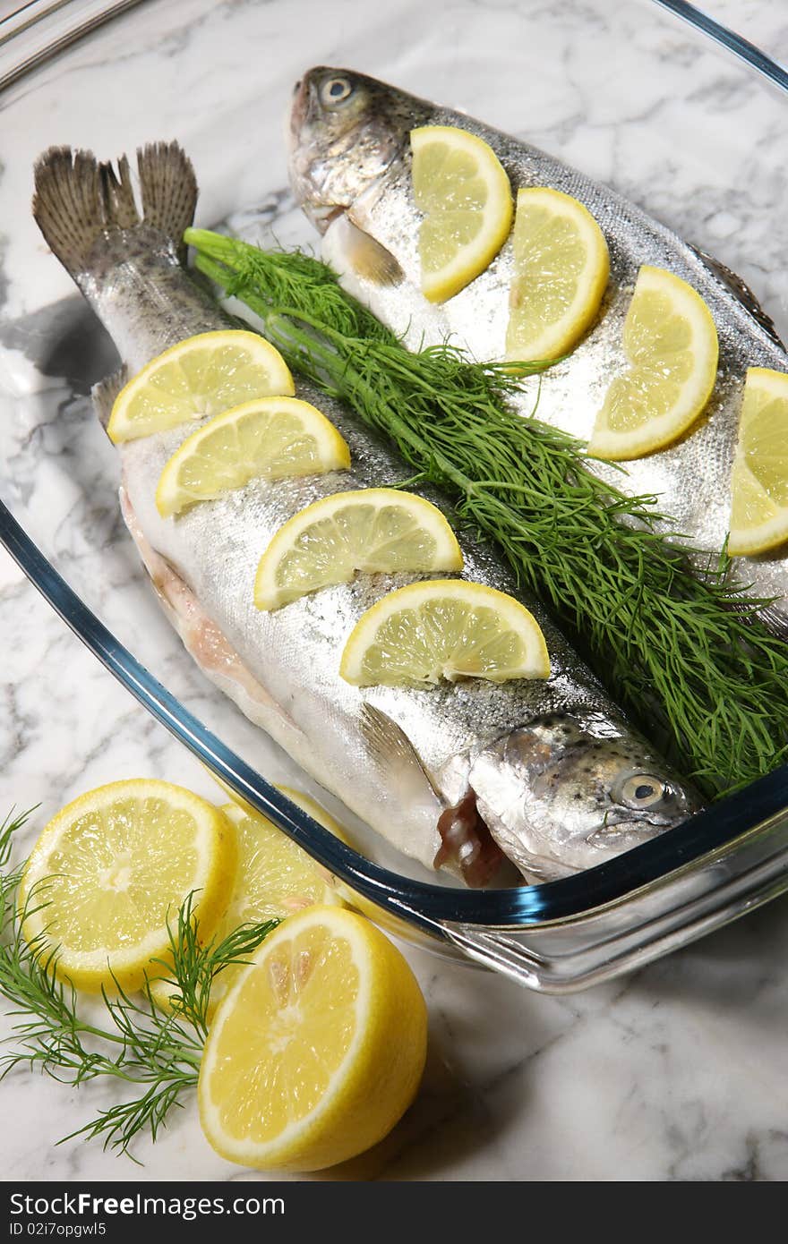 Fish on a white plate with lemons and dill on stone