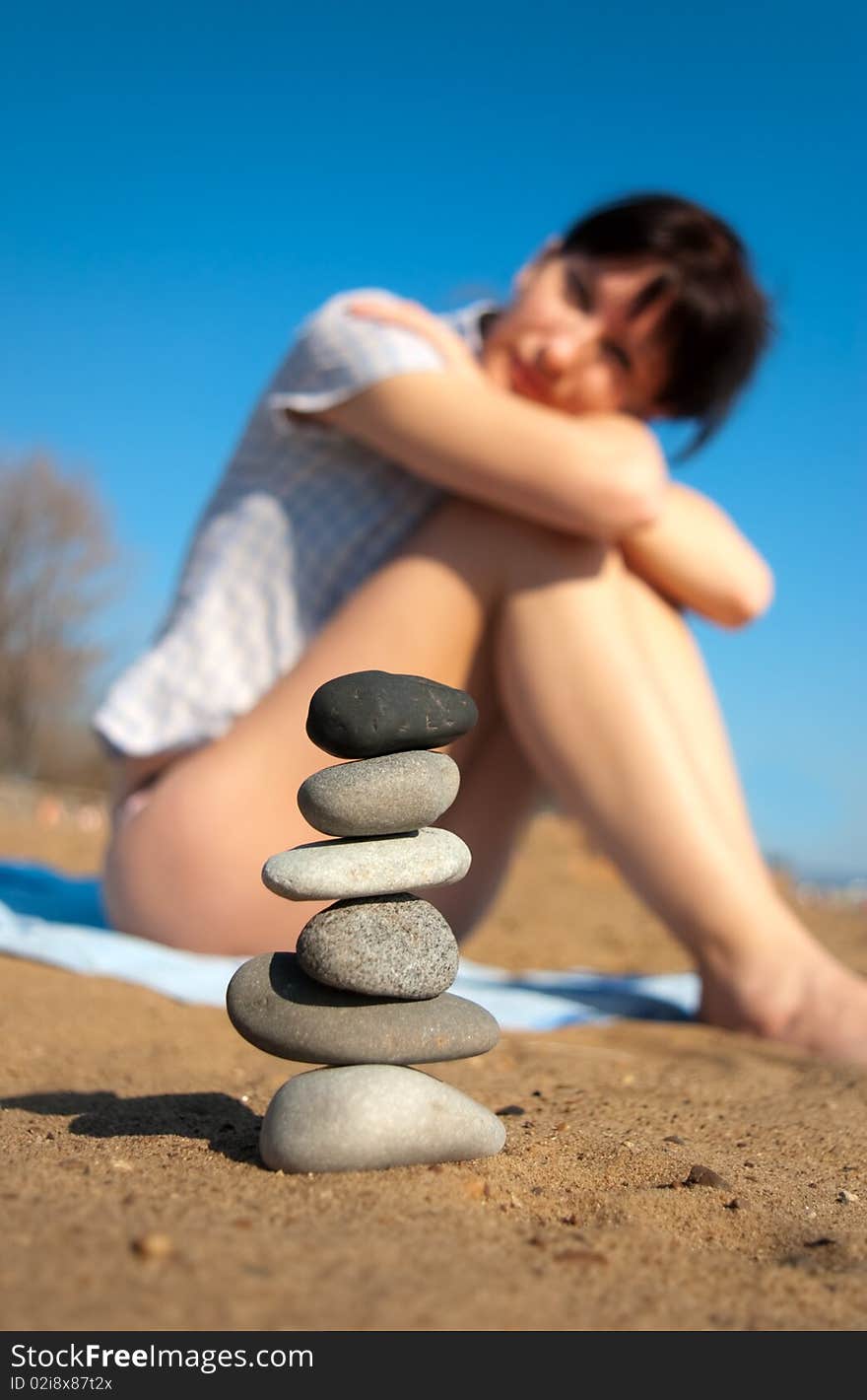 Young attractive woman sitting on the beach and looking at the stacked stones. Young attractive woman sitting on the beach and looking at the stacked stones