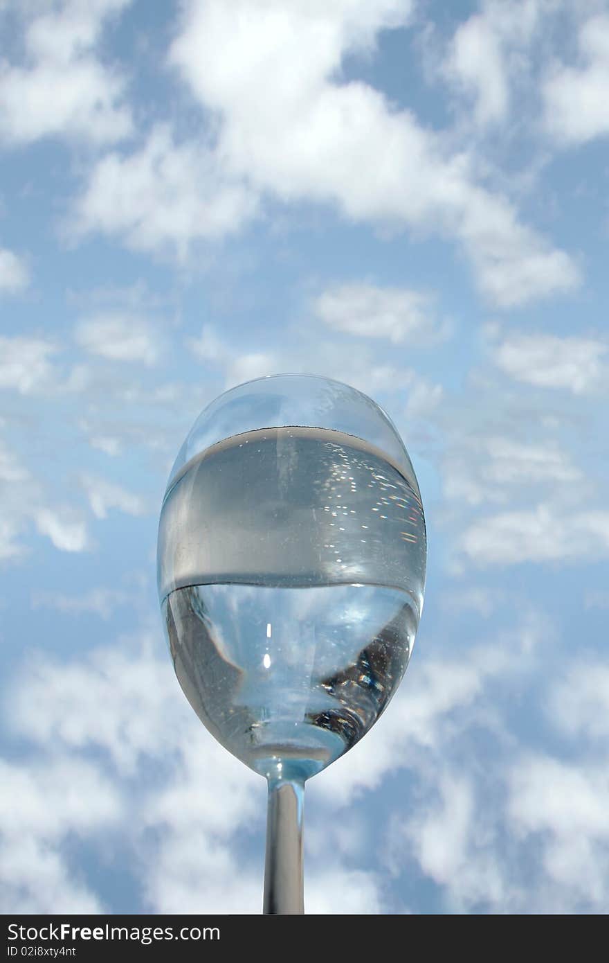 A glass of water against a bright cloudy blue sky background. A glass of water against a bright cloudy blue sky background