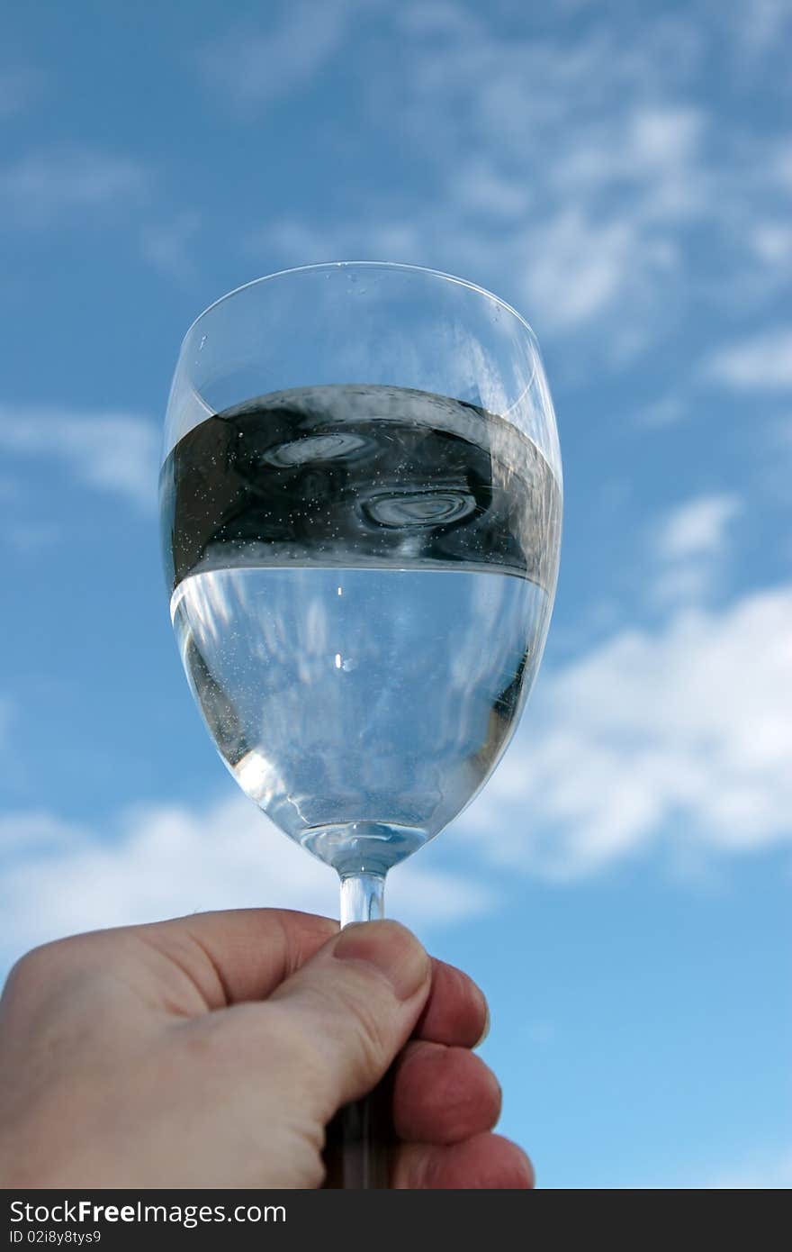 A glass of water held up in a toast against a bright cloudy blue sky background. A glass of water held up in a toast against a bright cloudy blue sky background