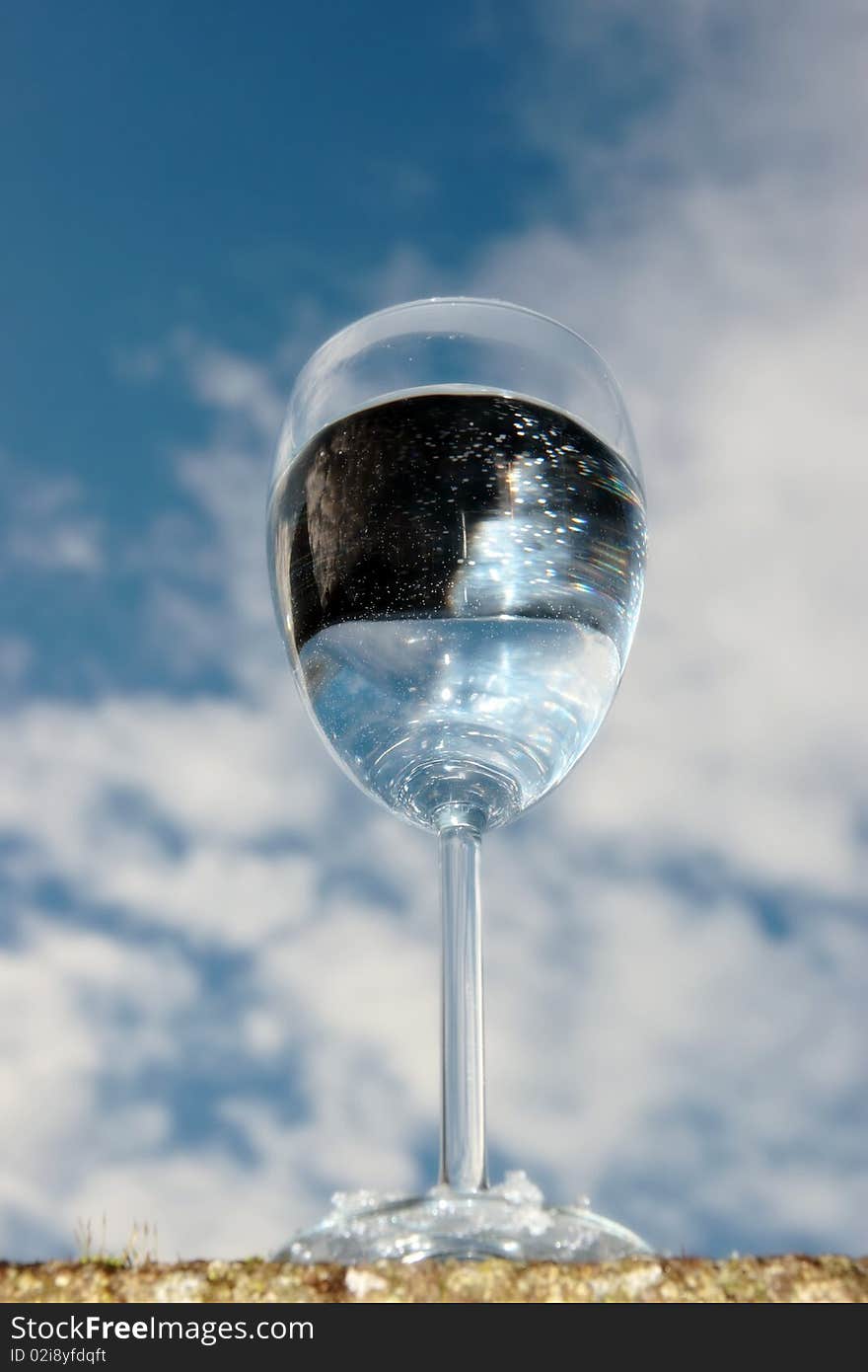 A glass of water on a wall against a bright cloudy blue sky background. A glass of water on a wall against a bright cloudy blue sky background