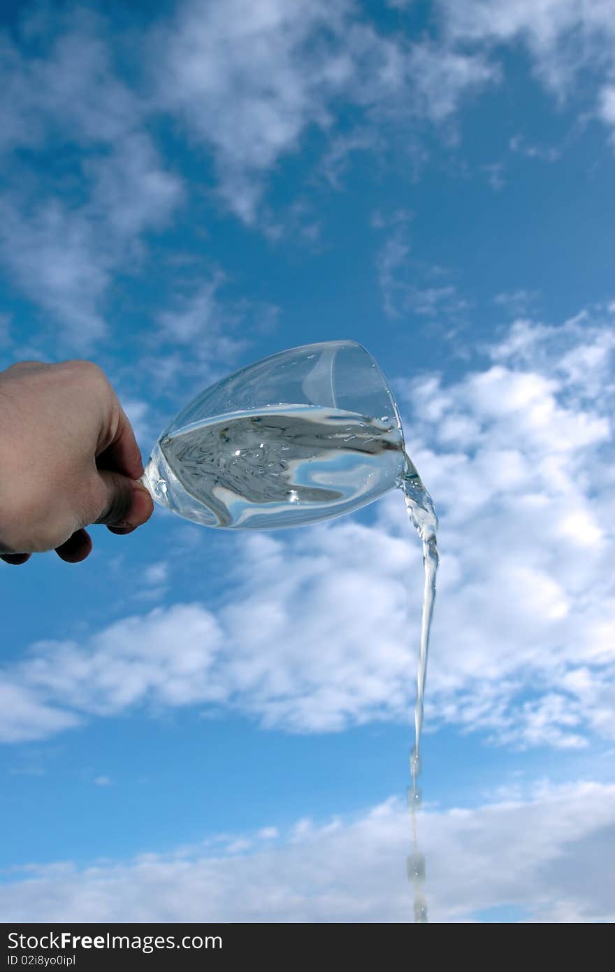 A glass of water being poured against a bright cloudy blue sky background. A glass of water being poured against a bright cloudy blue sky background