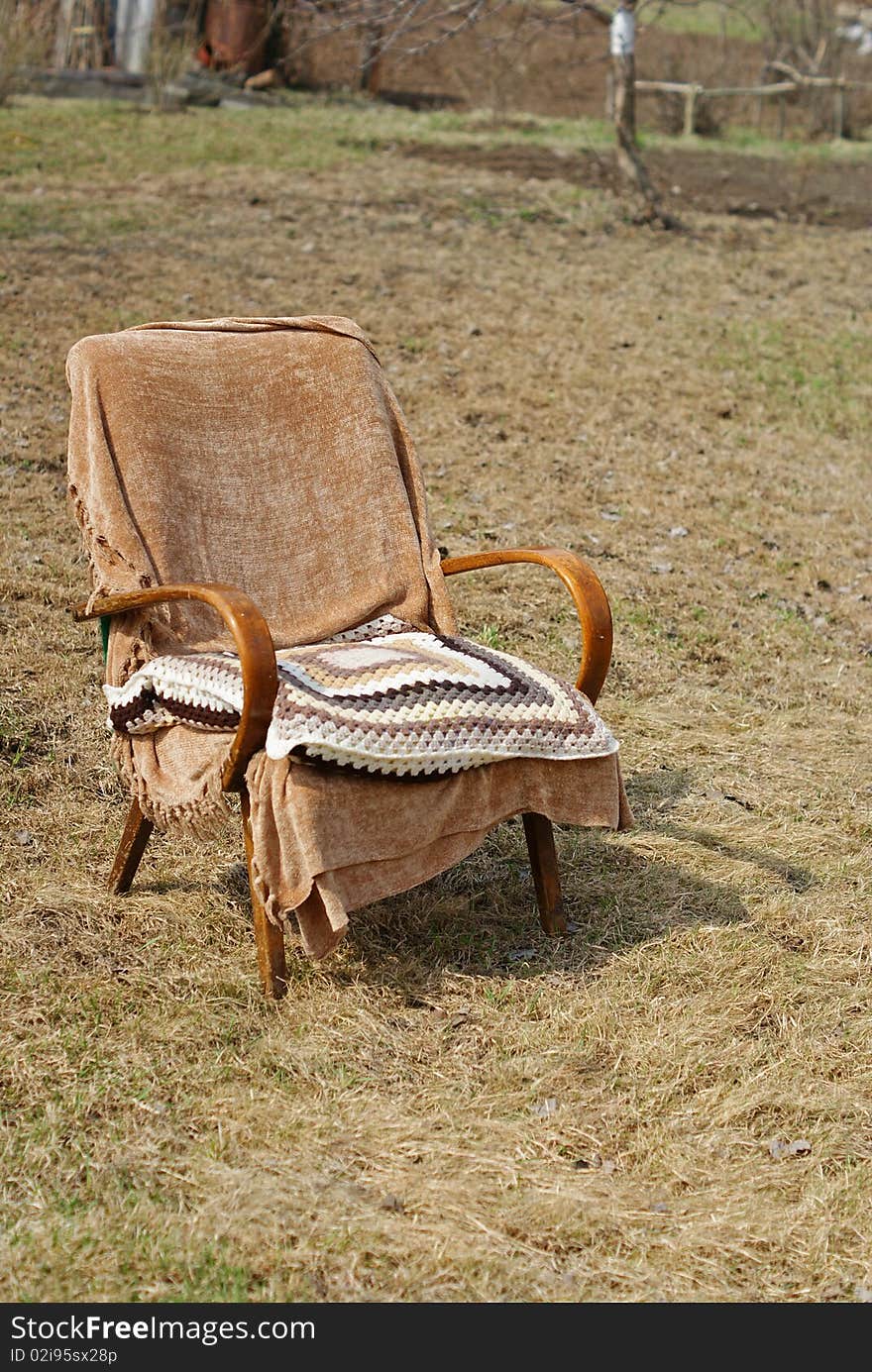 Old-fashioned brown garden chair with a textile cover and a wool knitted pillow. Old-fashioned brown garden chair with a textile cover and a wool knitted pillow