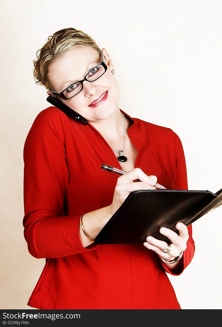 Business woman in red suit speaking on phone while writing in her folder. Business woman in red suit speaking on phone while writing in her folder