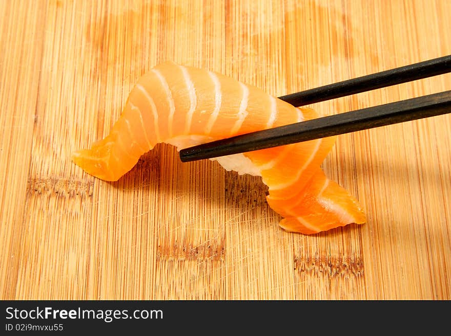 Close up of a piece of salmon nigiri being picked up with chop sticks. Close up of a piece of salmon nigiri being picked up with chop sticks