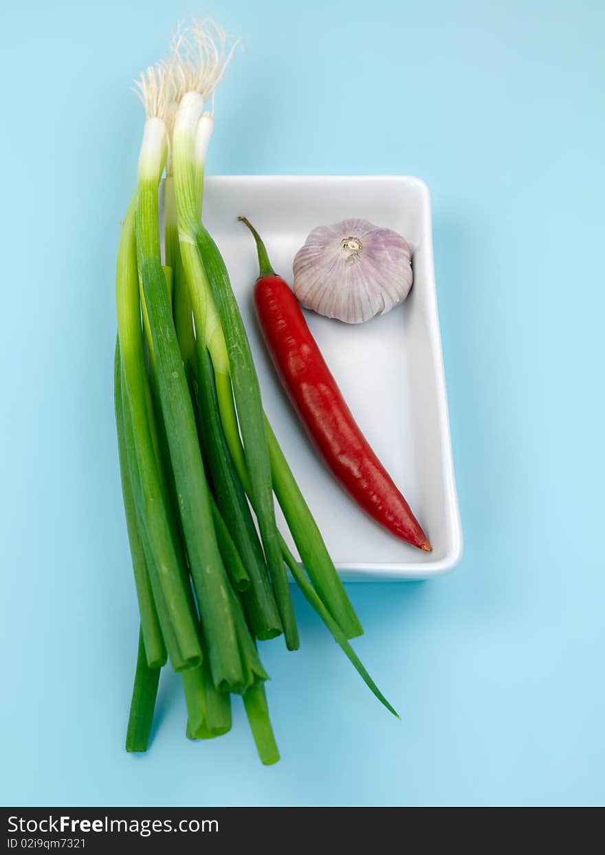 Spring onions, red pepper and garlic isolated against a blue background. Spring onions, red pepper and garlic isolated against a blue background