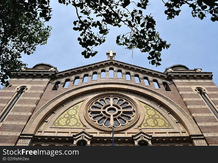 Looking up at a churches facade with stain glass and a cross on top.