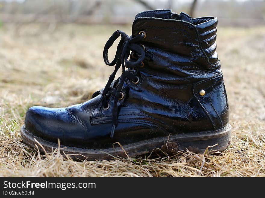 Dirty black boot on a dry grass background