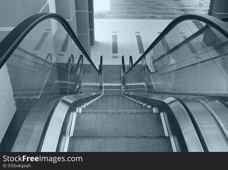 View of an escalator in an office building from above in blue tint. View of an escalator in an office building from above in blue tint