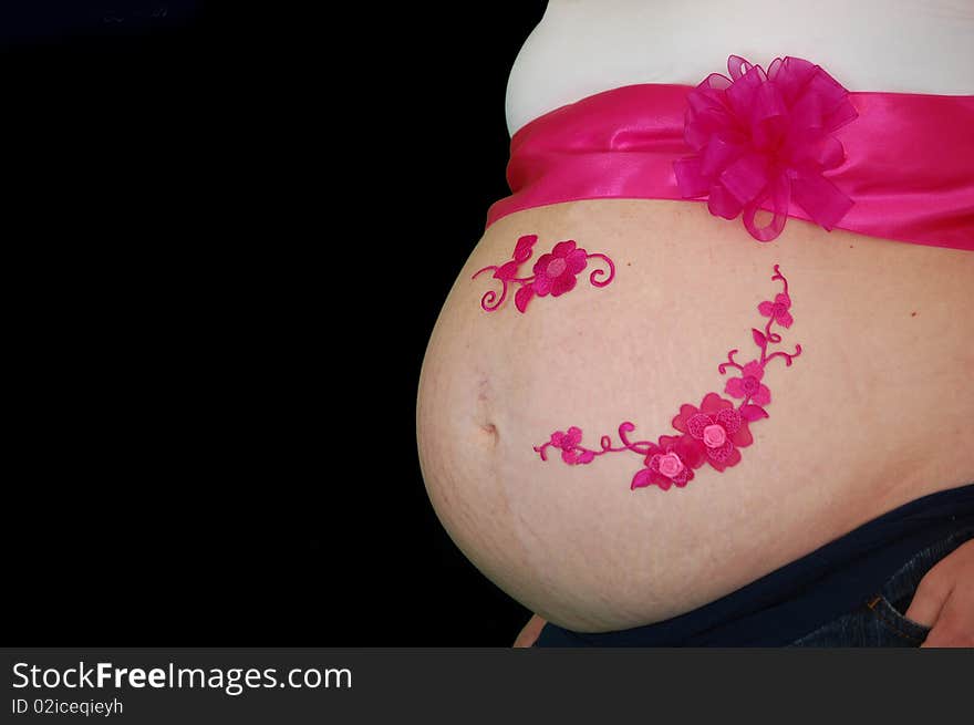 Pregnant belly wrapped in a pink bow and ribbon along with decorative flowers on a black backdrop isolated fushia bright belly button white shirt. Pregnant belly wrapped in a pink bow and ribbon along with decorative flowers on a black backdrop isolated fushia bright belly button white shirt