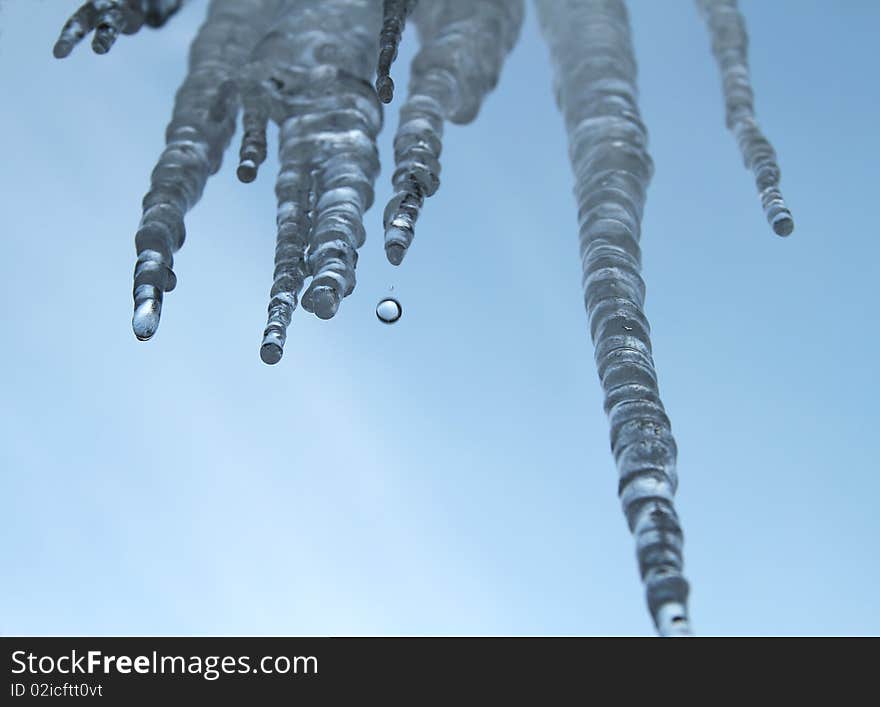 Icicles hanging against a blue sky with melting water dripping off of them. Icicles hanging against a blue sky with melting water dripping off of them.