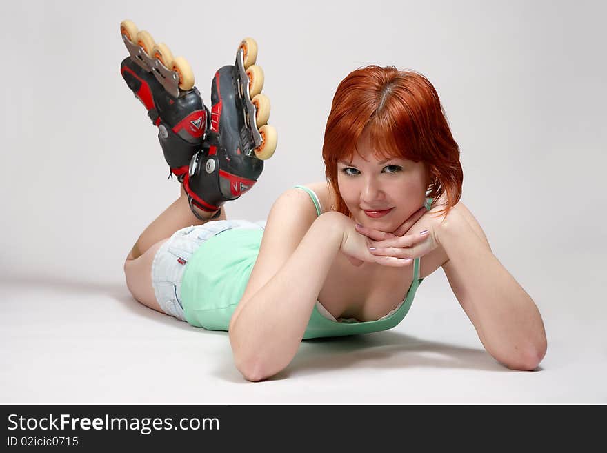 Smiling beautiful young woman on roller-skates lying on the floor , on white background. Studio shot