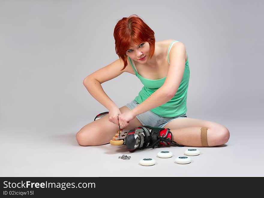 Young woman sitting on the floor and repair roller-skates. Studio shot on white background. Young woman sitting on the floor and repair roller-skates. Studio shot on white background.