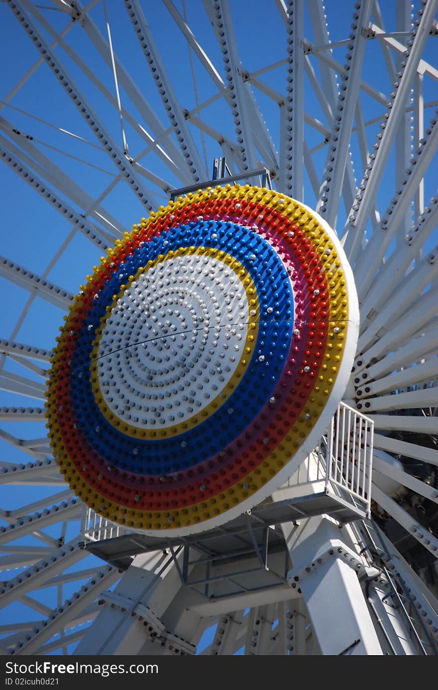 A rainbow circle of lights in daylight that is in the center of a ferris wheel ride. A rainbow circle of lights in daylight that is in the center of a ferris wheel ride.