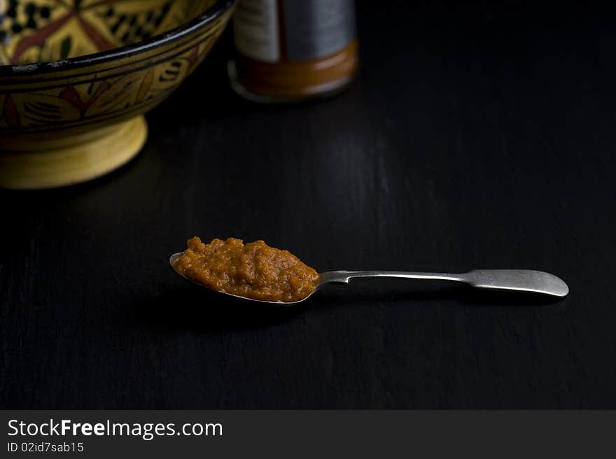 A Spoonful of Harissa Paste In Front of A Moroccan Dish On A Slate Worktop,. A Spoonful of Harissa Paste In Front of A Moroccan Dish On A Slate Worktop,