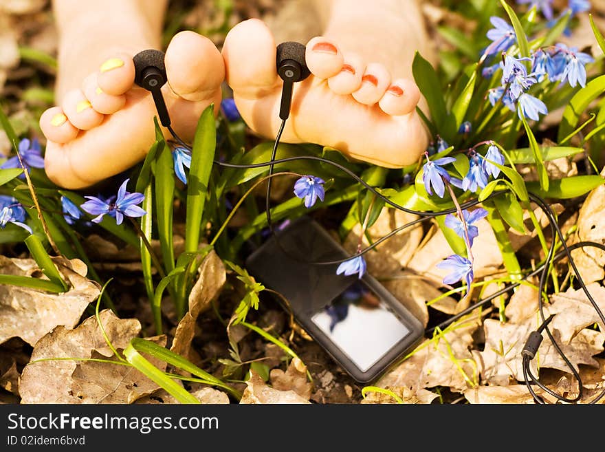 Barefooted tender woman's feet listening mp3 player in snowdrops. Barefooted tender woman's feet listening mp3 player in snowdrops