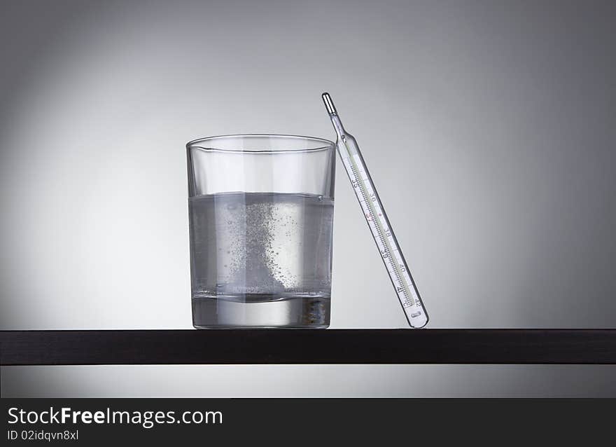 Glass with thermometer on gray background