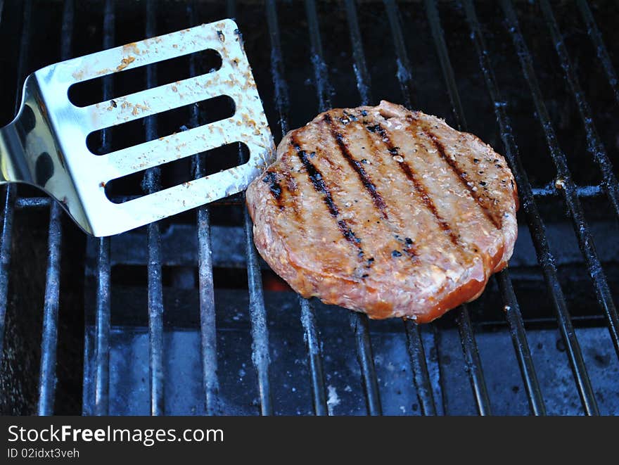 Spatula flipping hamburger on grill