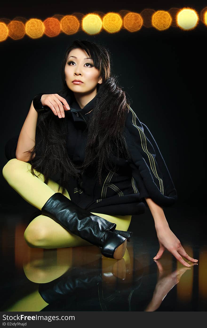 Sitting brunette asian model on black background with night light reflections