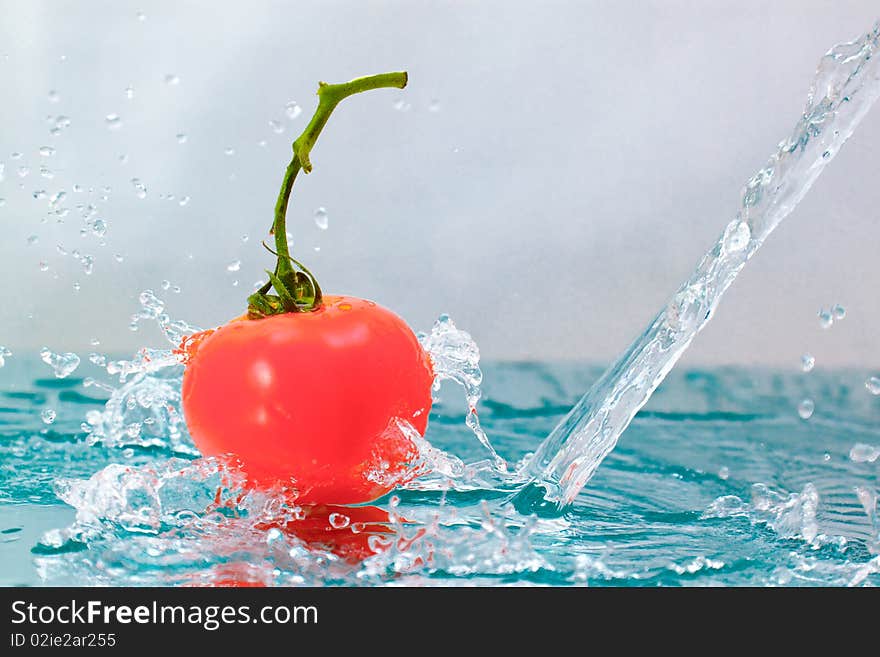 Red tomato with green stalk and splash water over white background