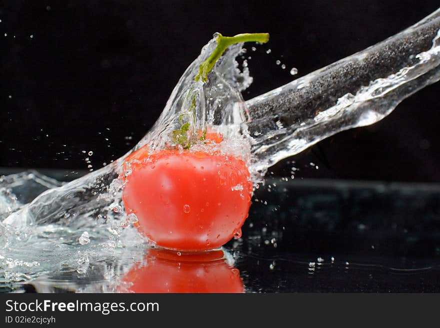 Red tomato with green stalk and splash water over black background