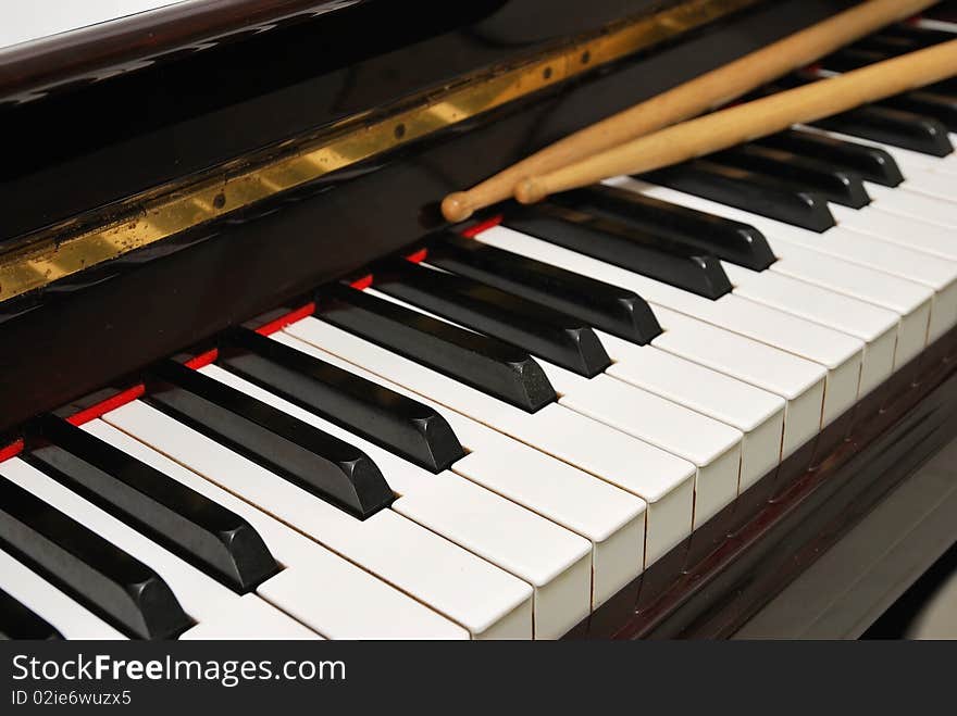 Diagonal shot of drum sticks on piano keyboard