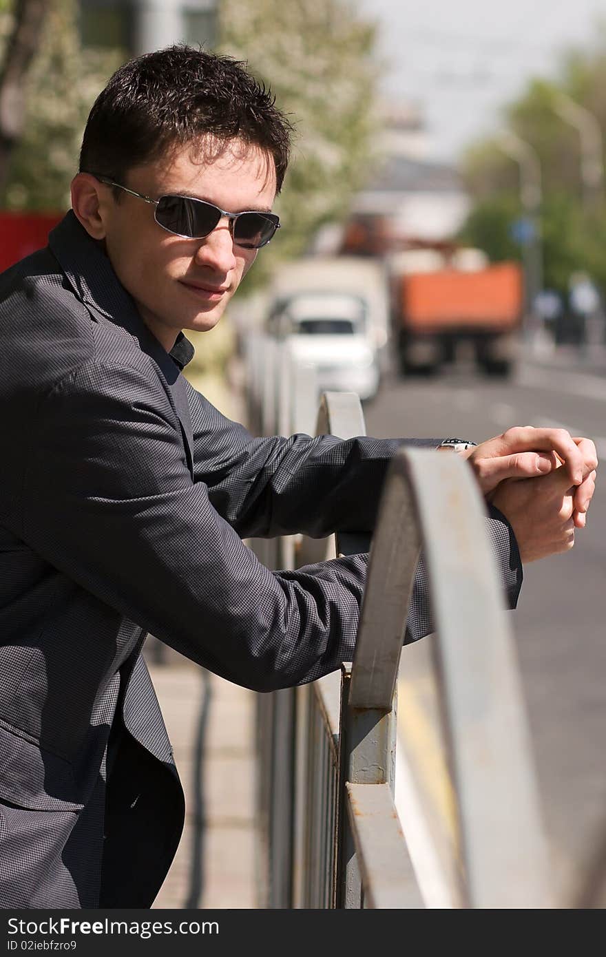 Young guy in black sunglasses waiting for someone near the road in the middle of a day. Young guy in black sunglasses waiting for someone near the road in the middle of a day