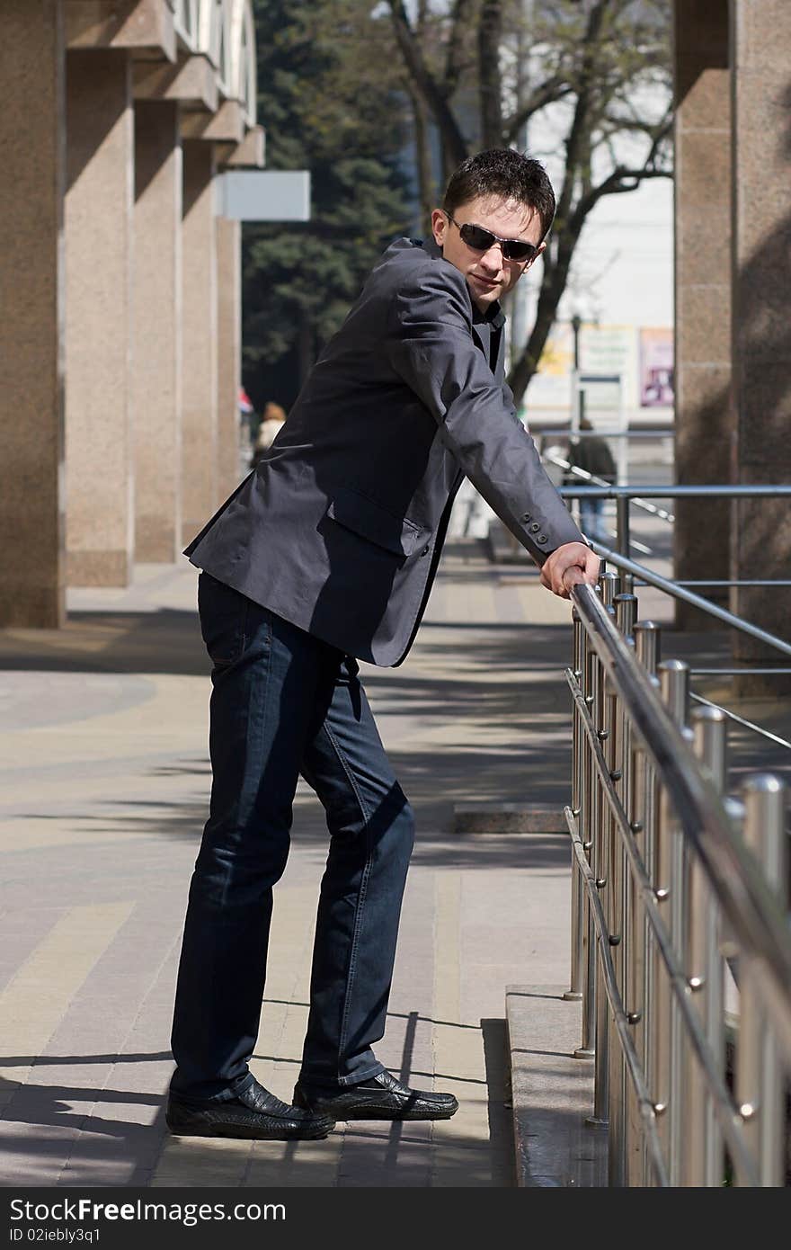 Young businessman leans on metal handrails near the office building with columns. Young businessman leans on metal handrails near the office building with columns